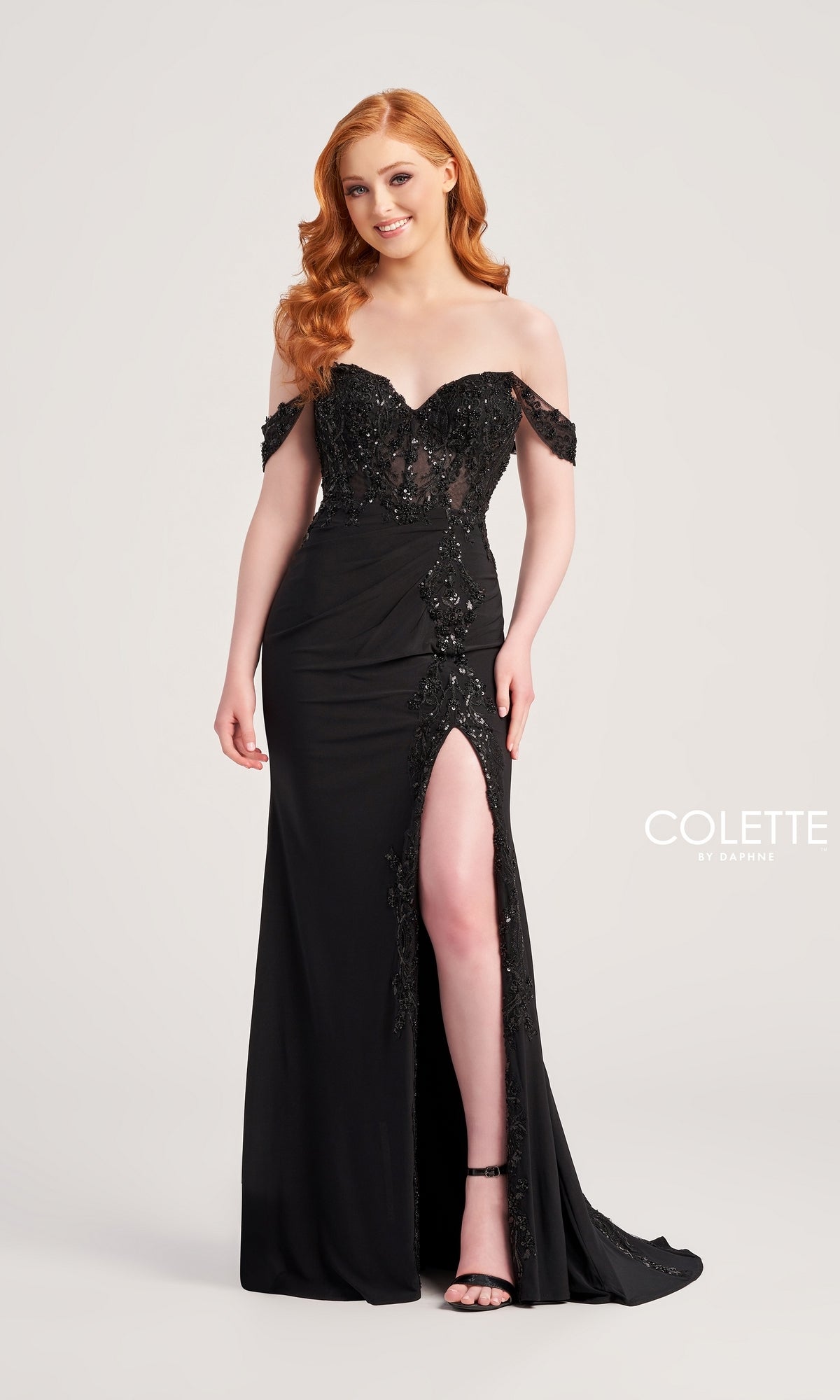 A woman with long red hair wears the Colette Off-Shoulder Long Formal Prom Dress CL5276 in black, featuring beaded lace applique and a high slit, standing against a plain background.